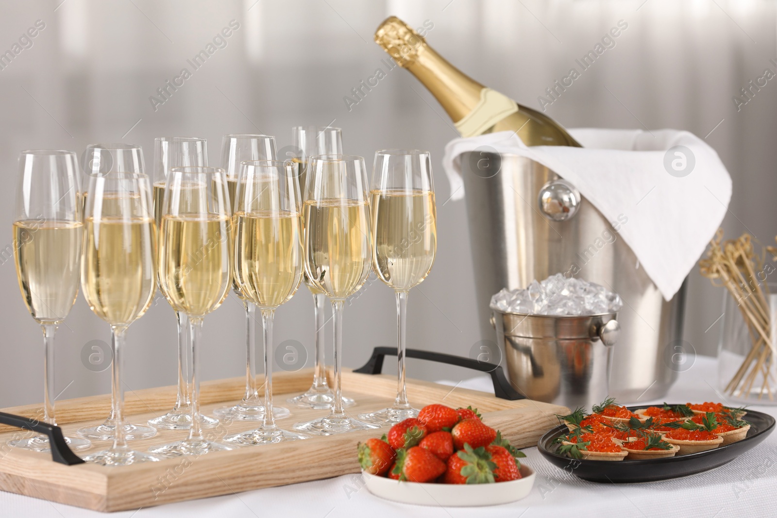 Photo of Champagne, ice bucket, strawberries and canapes with red caviar on white table indoors