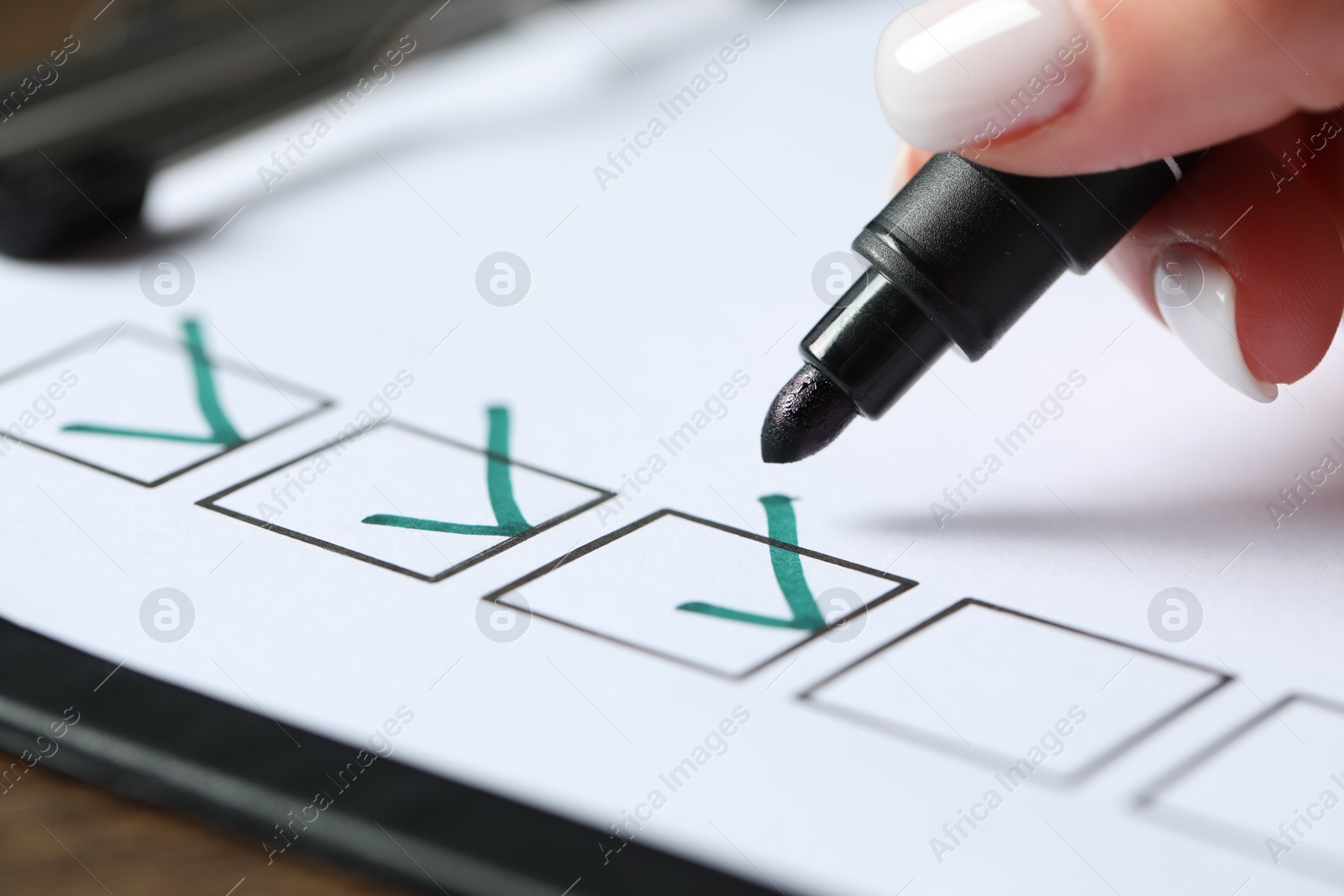 Photo of Woman checking box of paper form at wooden table, closeup