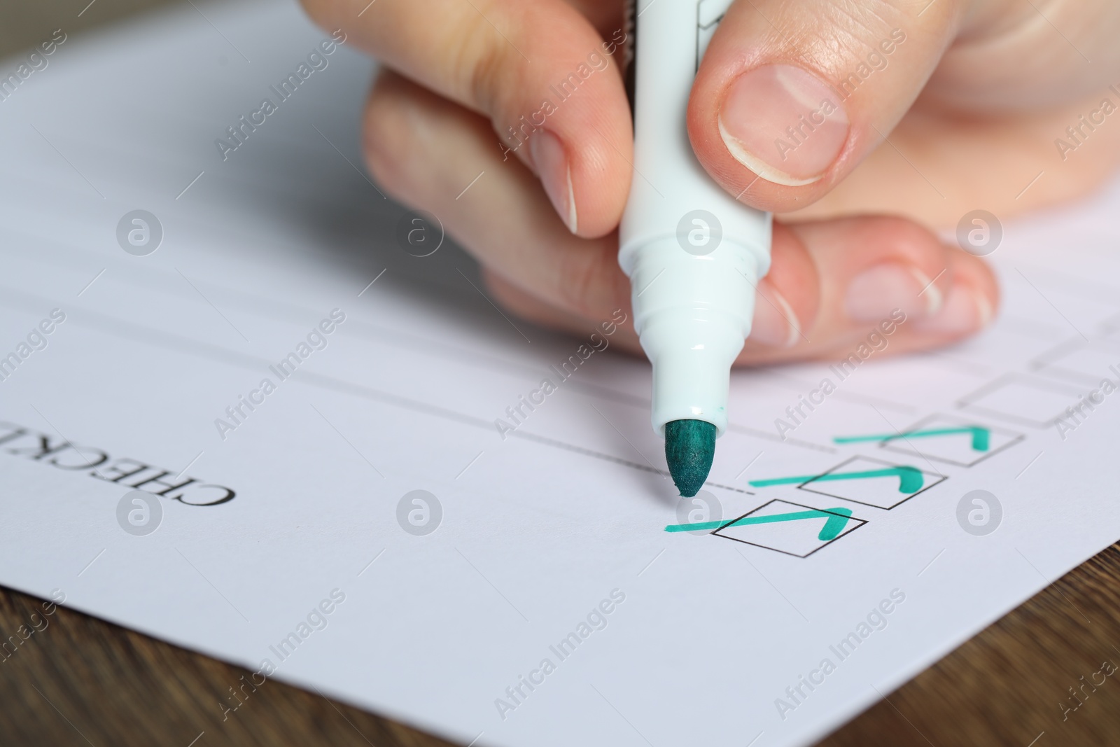 Photo of Woman checking box of paper form at wooden table, closeup