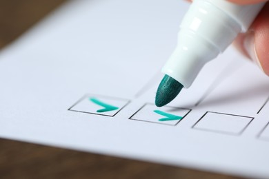 Photo of Woman checking box of paper form at table, closeup