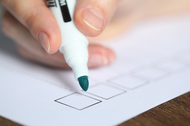 Photo of Woman checking box of paper form at wooden table, closeup