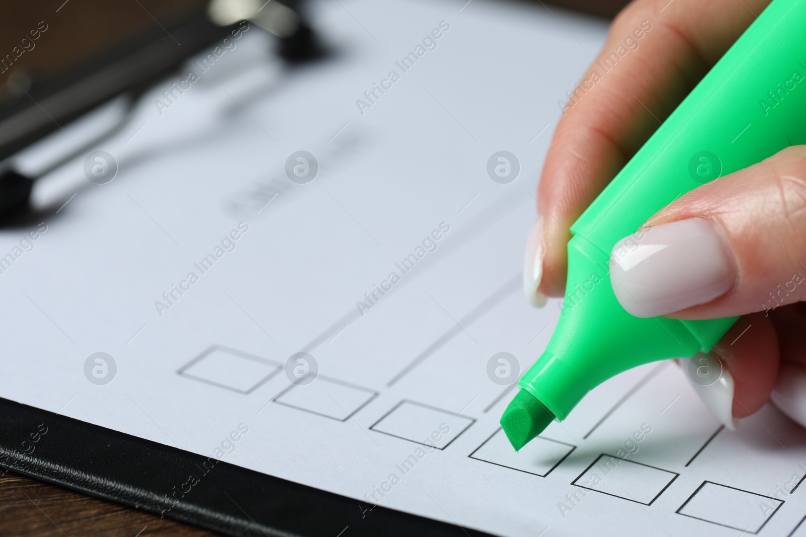 Photo of Woman checking box of paper form at wooden table, closeup