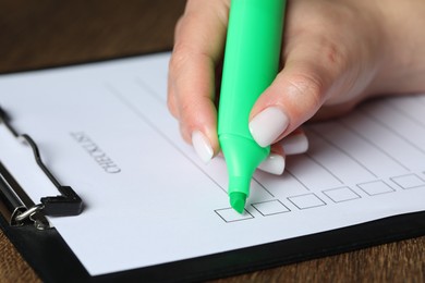 Photo of Woman checking box of paper form at wooden table, closeup