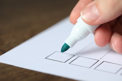 Photo of Woman checking box of paper form at wooden table, closeup