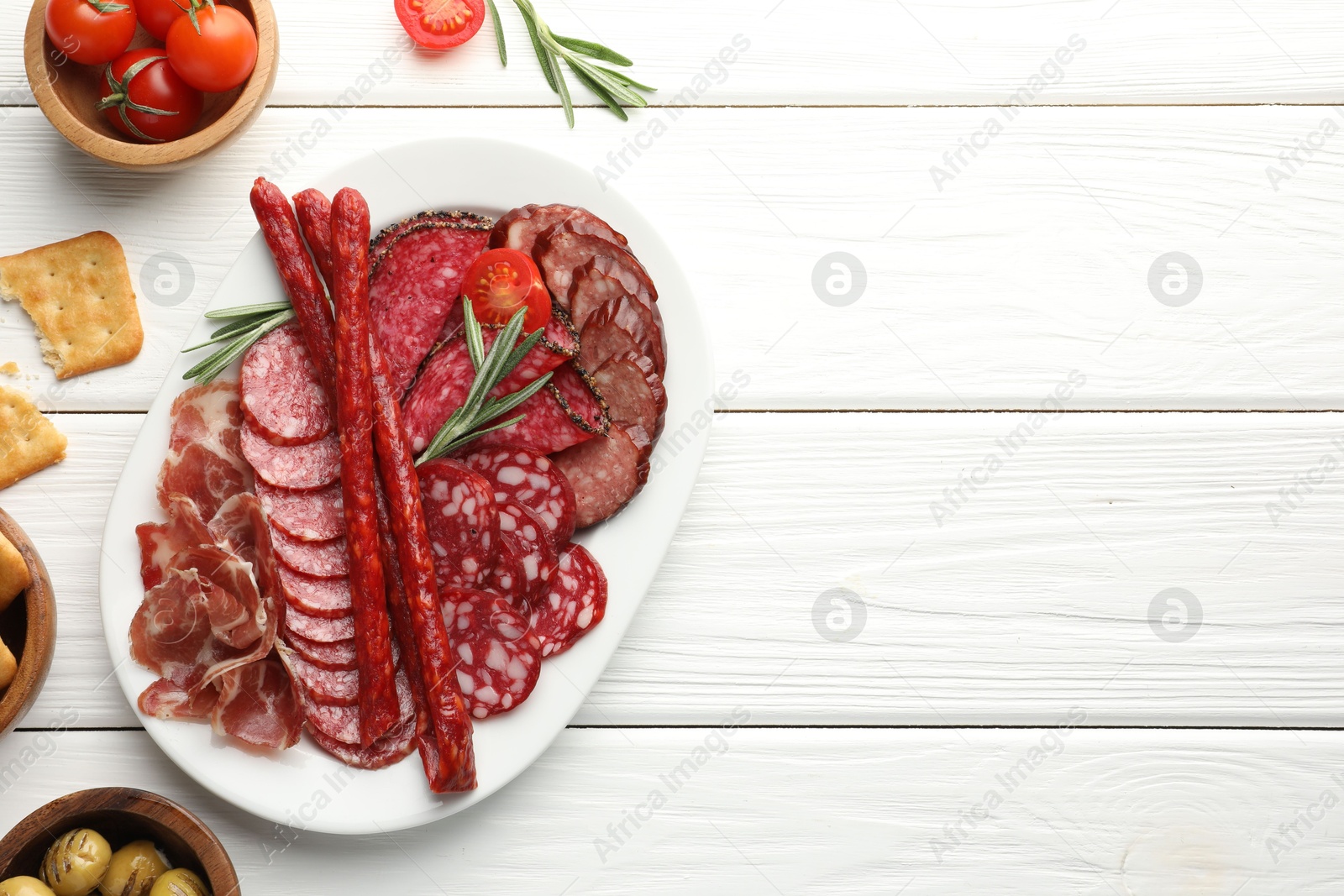 Photo of Different smoked sausages slices served on white wooden table, flat lay. Space for text