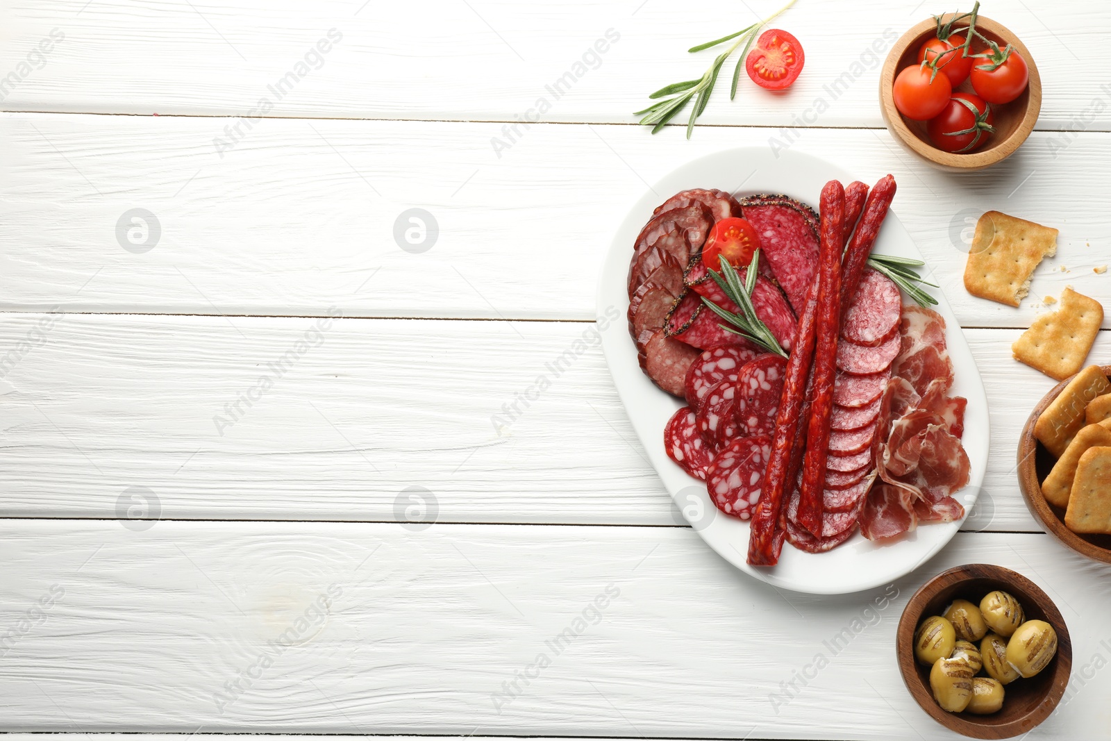 Photo of Different smoked sausages slices served on white wooden table, flat lay. Space for text