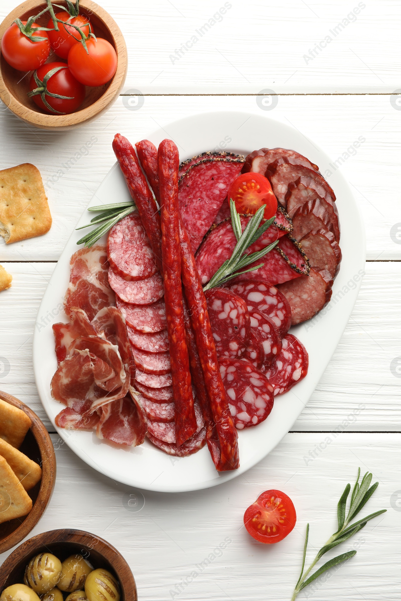 Photo of Different smoked sausages slices served on white wooden table, flat lay