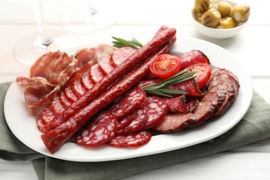 Photo of Different smoked sausages slices served on white wooden table, closeup