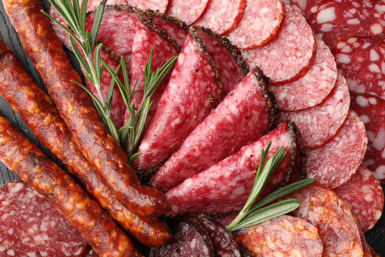 Photo of Different smoked sausages slices and rosemary on table, closeup