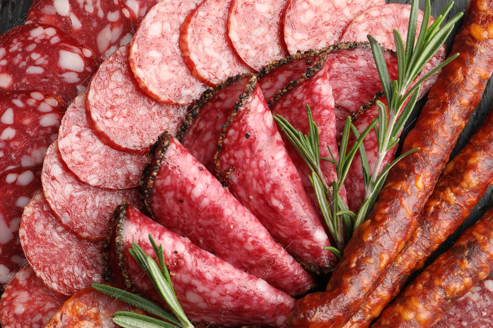 Photo of Different smoked sausages slices and rosemary on table, closeup