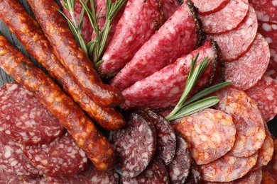 Photo of Different smoked sausages slices and rosemary on table, closeup