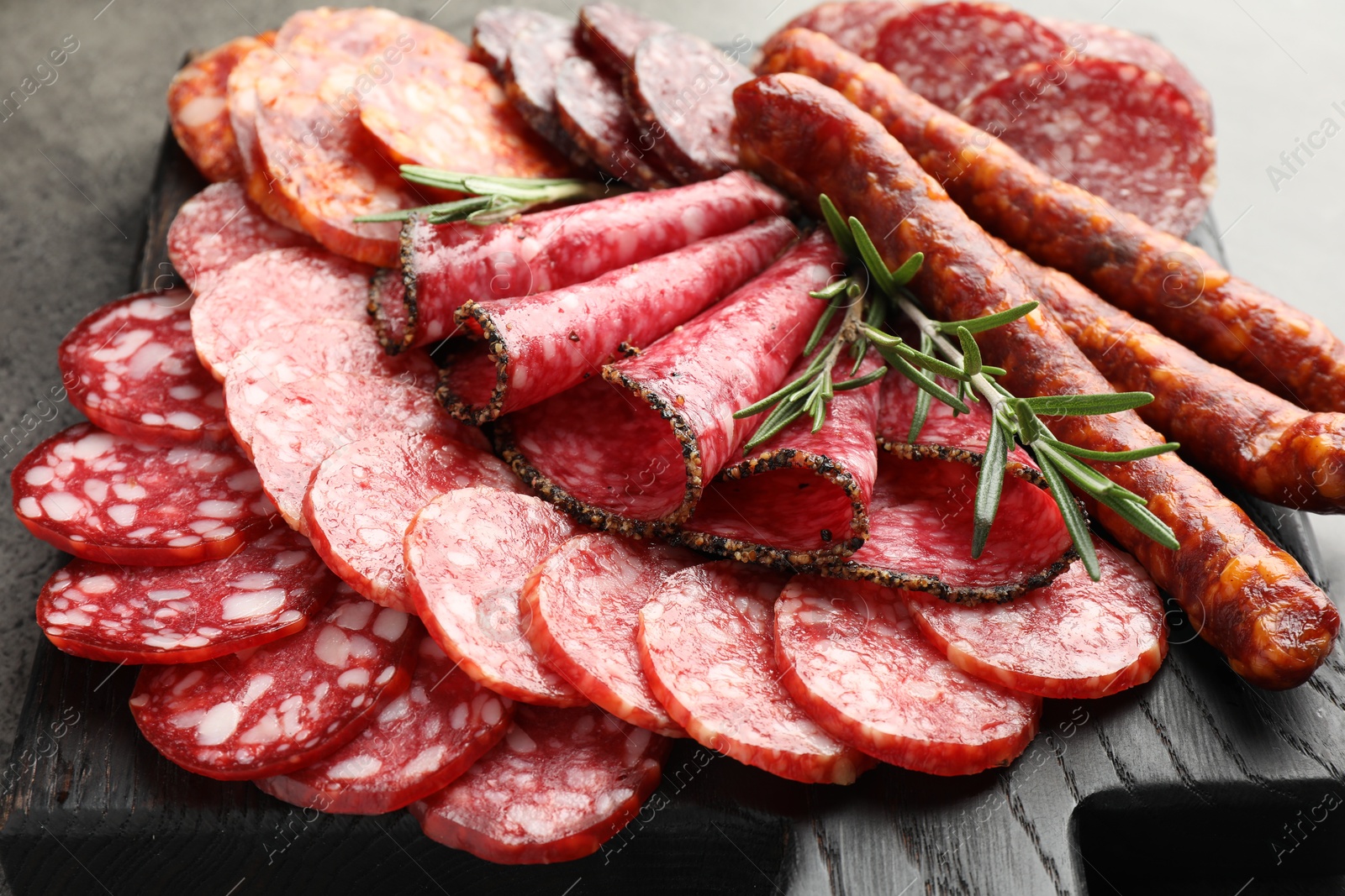 Photo of Different smoked sausages slices served on grey table, closeup