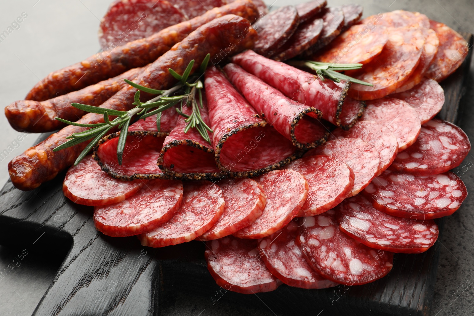 Photo of Different smoked sausages slices served on grey table, closeup