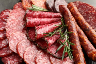 Photo of Different smoked sausages slices and rosemary on table, closeup