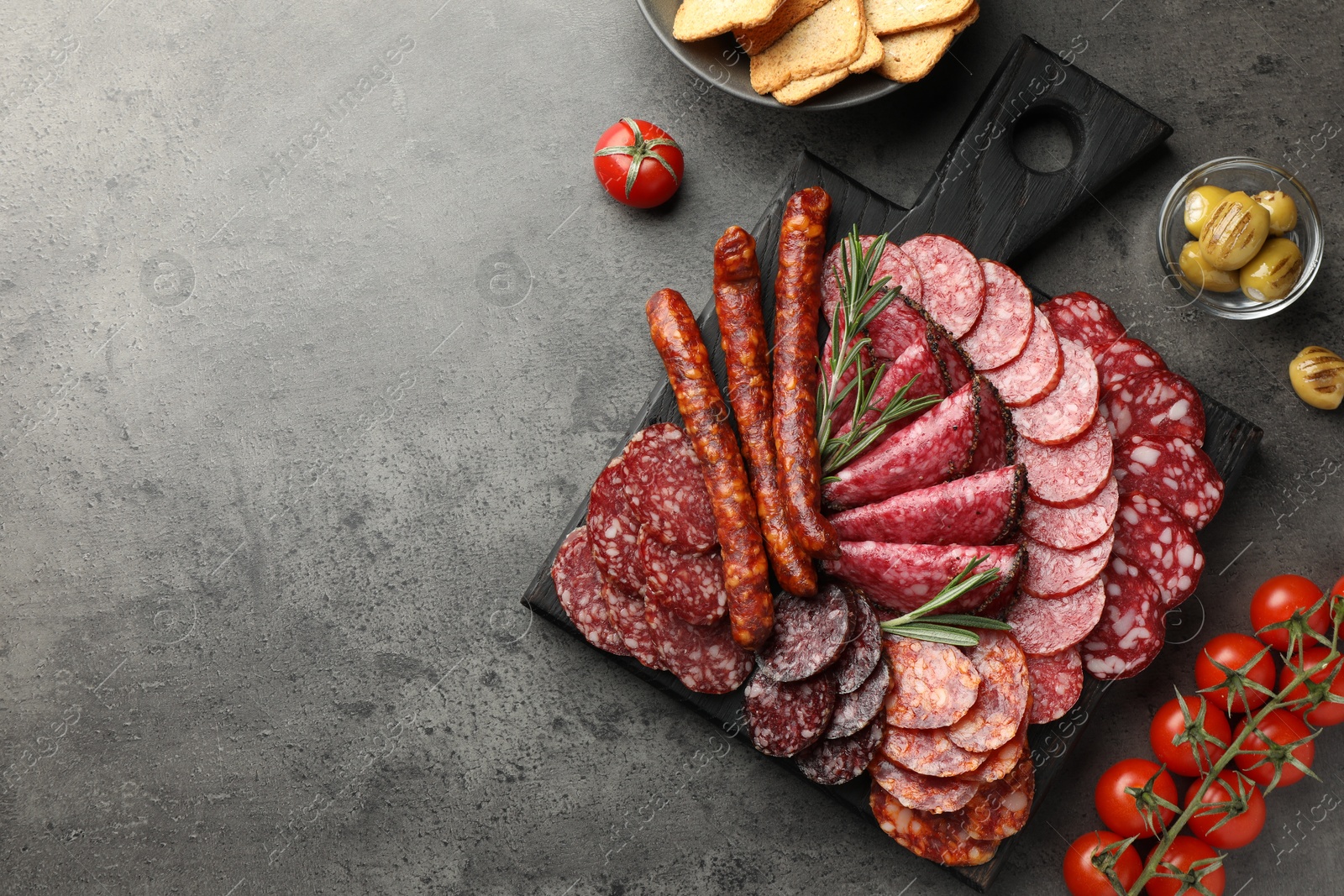 Photo of Different smoked sausages slices served on grey table, flat lay. Space for text