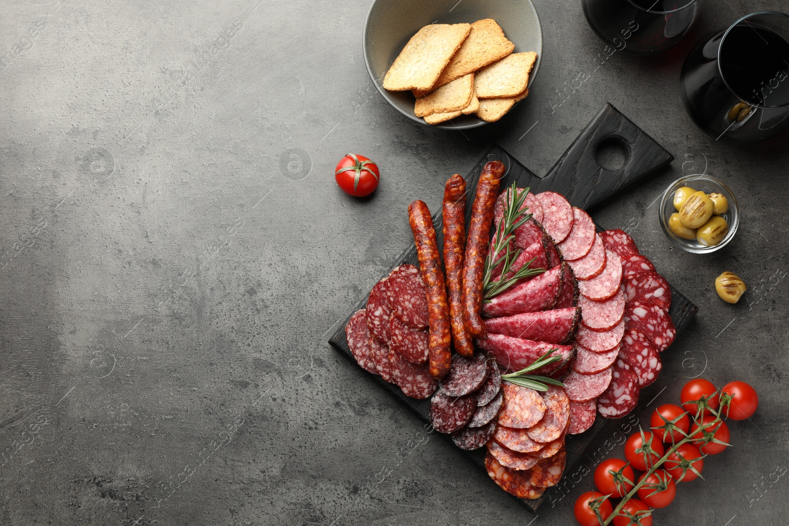 Photo of Different smoked sausages slices served on grey table, flat lay. Space for text