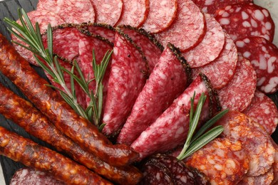 Photo of Different smoked sausages slices and rosemary on table, closeup