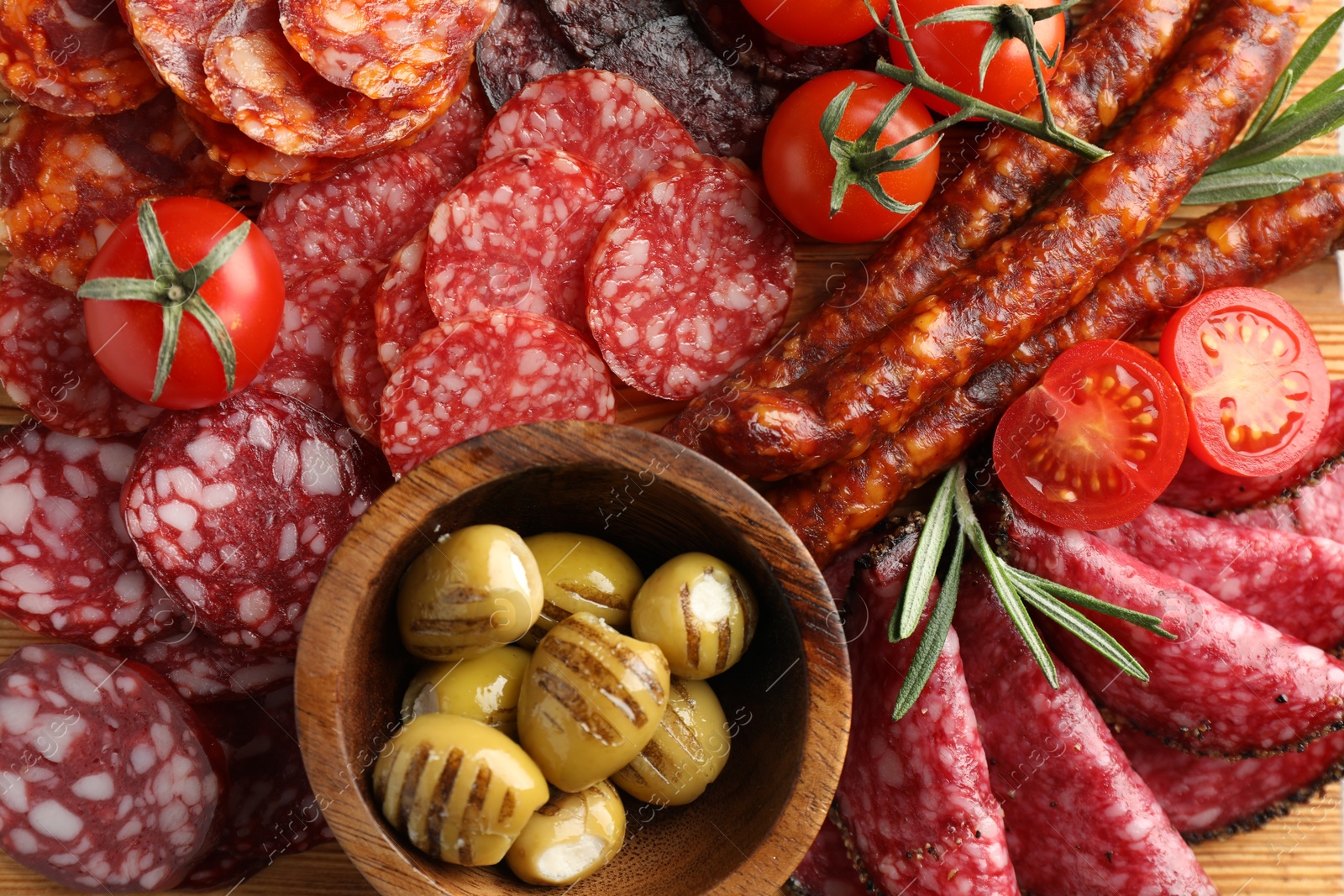 Photo of Different smoked sausages slices, olives, tomatoes and rosemary on table, closeup