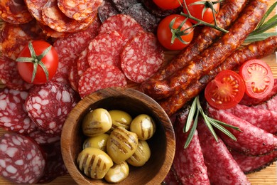 Photo of Different smoked sausages slices, olives, tomatoes and rosemary on table, closeup