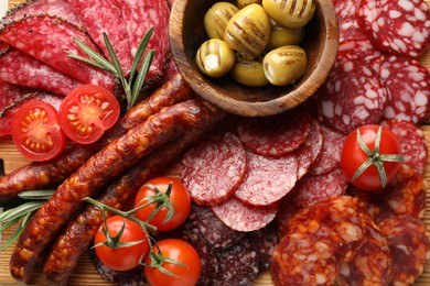 Photo of Different smoked sausages slices, olives, tomatoes and rosemary on table, closeup