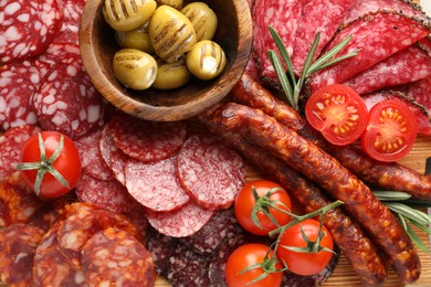 Photo of Different smoked sausages slices, olives, tomatoes and rosemary on table, closeup