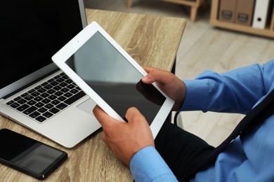 Photo of Businessman with tablet, laptop and smartphone at wooden table, closeup. Modern technology