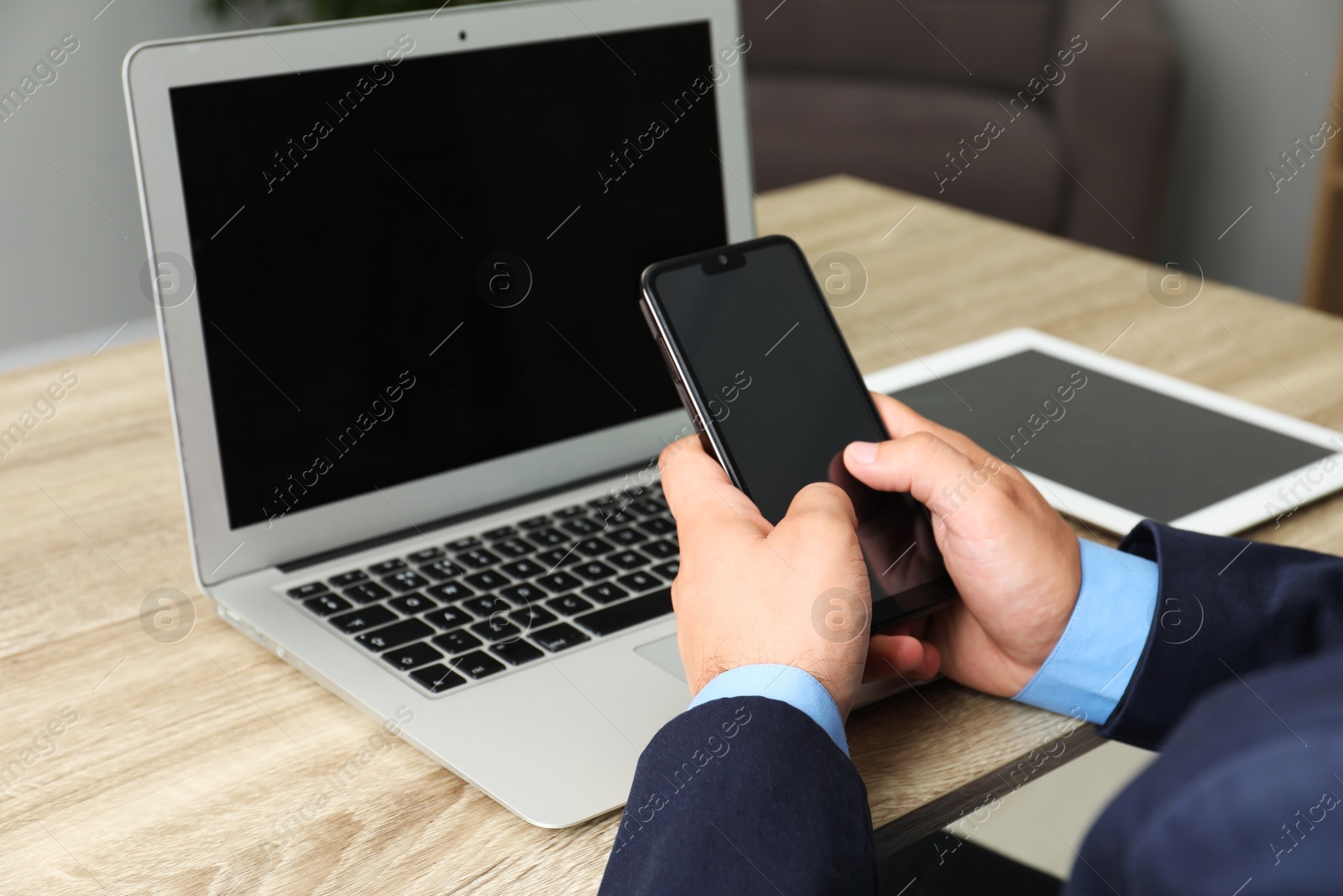 Photo of Businessman using smartphone near laptop at wooden table, closeup. Modern technology