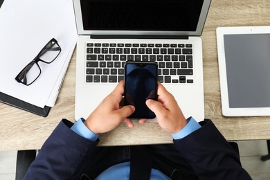 Photo of Businessman using smartphone near laptop at wooden table, top view. Modern technology