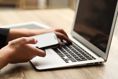 Photo of Businessman using laptop and smartphone at wooden table, closeup. Modern technology