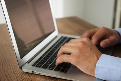 Photo of Businessman using laptop at wooden table, closeup. Modern technology