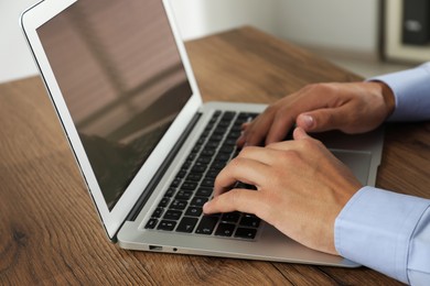 Photo of Businessman using laptop at wooden table, closeup. Modern technology