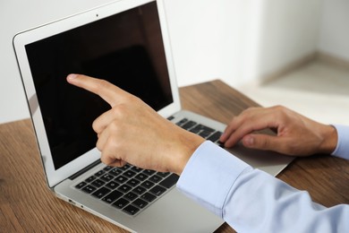 Photo of Businessman using laptop at wooden table, closeup. Modern technology