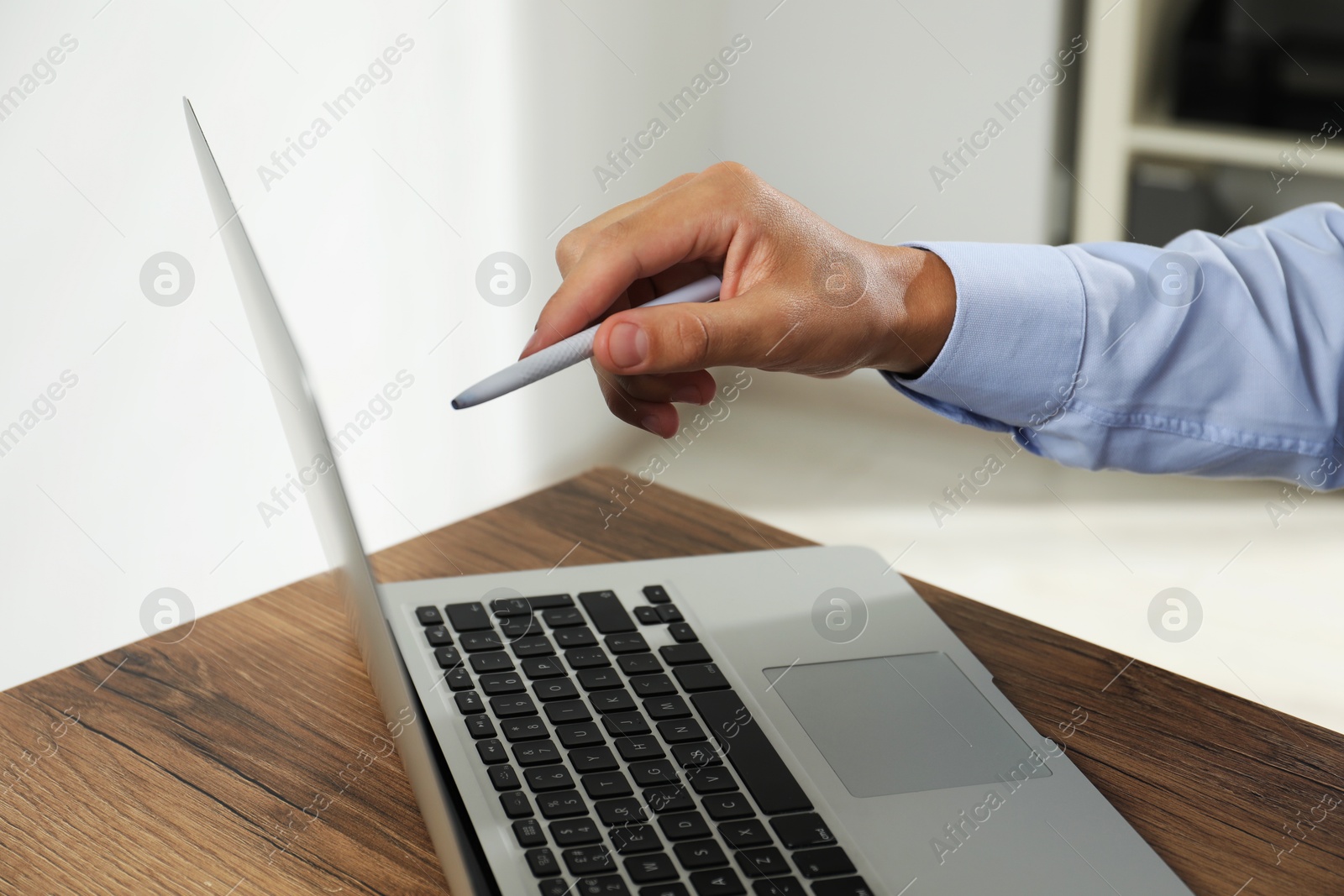 Photo of Businessman with pen near laptop at wooden table, closeup. Modern technology