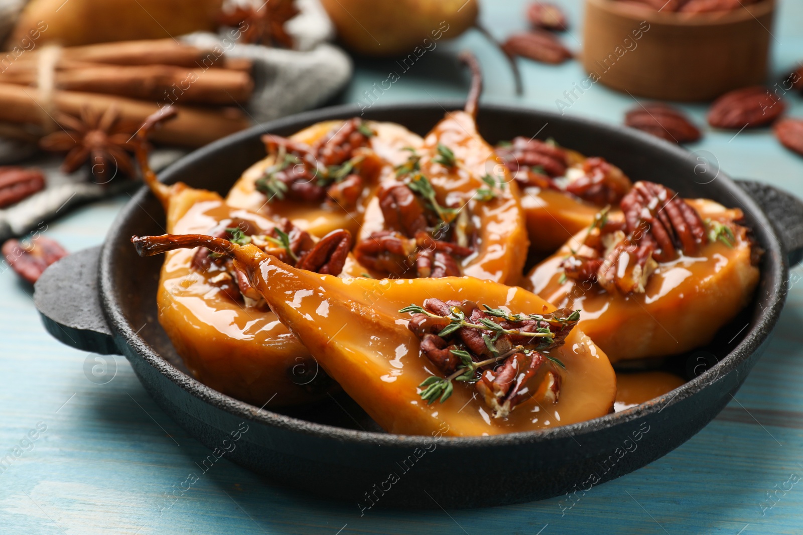 Photo of Delicious pears with caramel sauce, pecan nuts and thyme on light blue wooden table, closeup