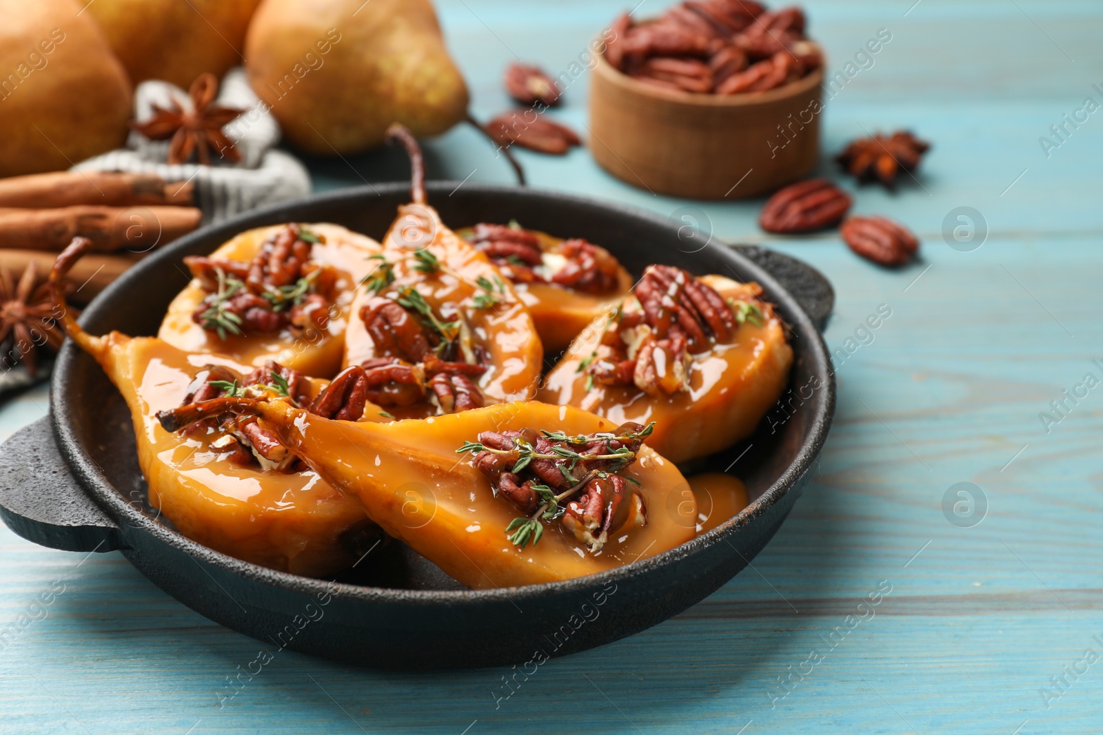 Photo of Delicious pears with caramel sauce, pecan nuts and thyme on light blue wooden table, closeup