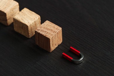 Photo of Magnet attracting cubes on black wooden table, closeup