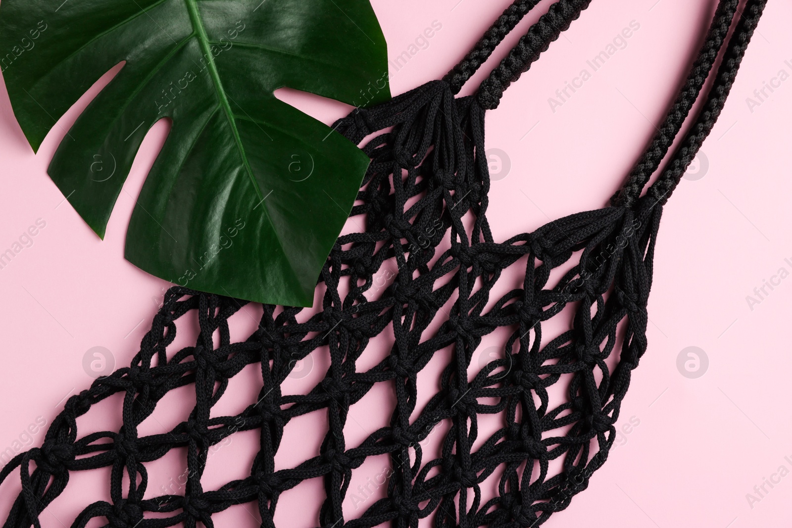 Photo of Macrame shopping bag and monstera leaf on pink background, top view