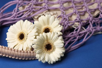 Photo of Macrame shopping bag with flowers on blue background, closeup