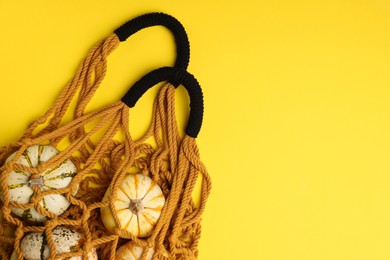 Photo of Macrame shopping bag with pumpkins on yellow background, top view. Space for text