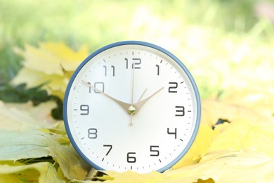 Photo of Autumn time. Alarm clock among fallen leaves, closeup