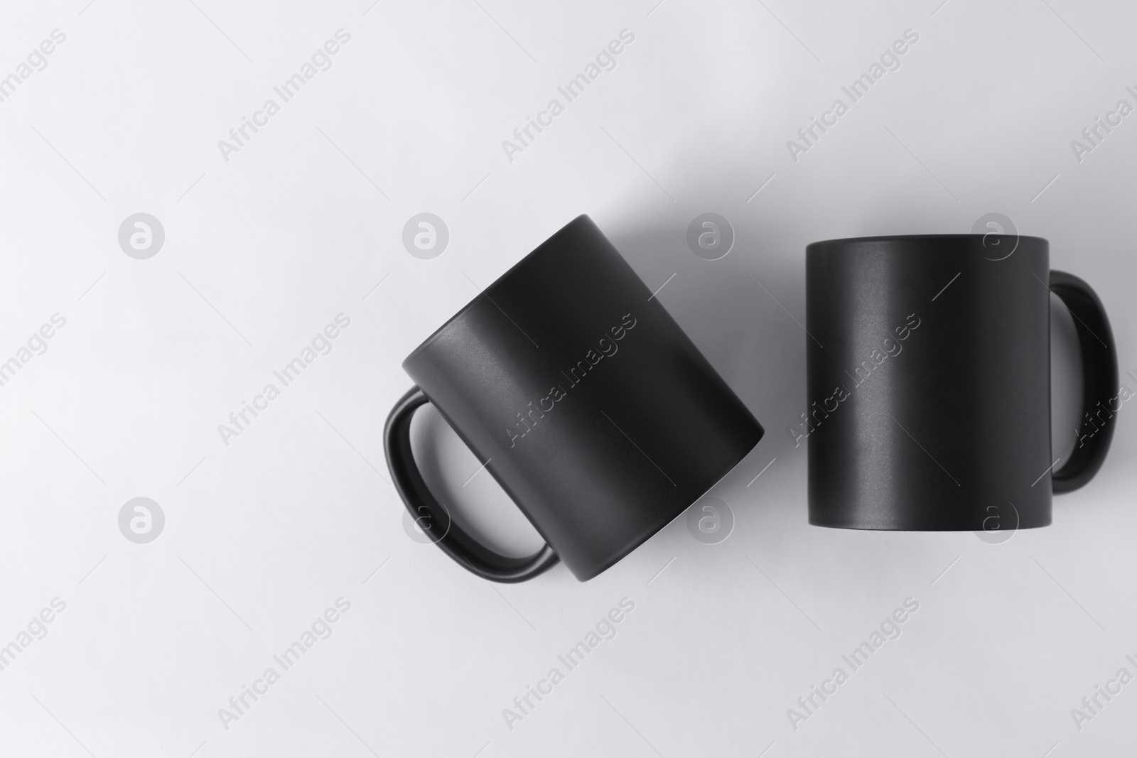 Photo of Two blank black mugs on white background, top view. Mockup for design