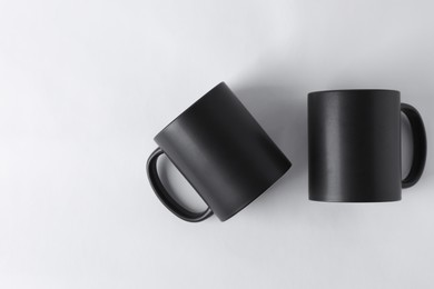 Photo of Two blank black mugs on white background, top view. Mockup for design