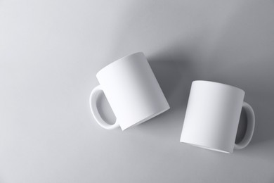 Photo of Two blank white mugs on light background, top view. Mockup for design