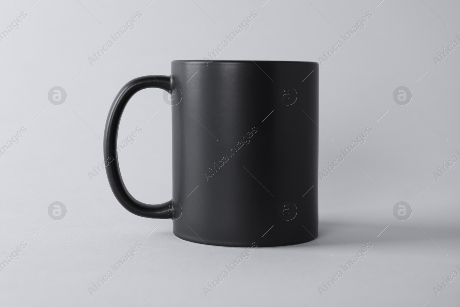 Photo of One blank black mug on light background. Mockup for design