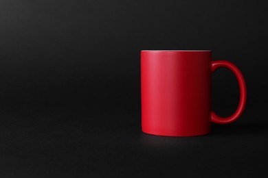 Photo of One blank red mug on black background. Mockup for design