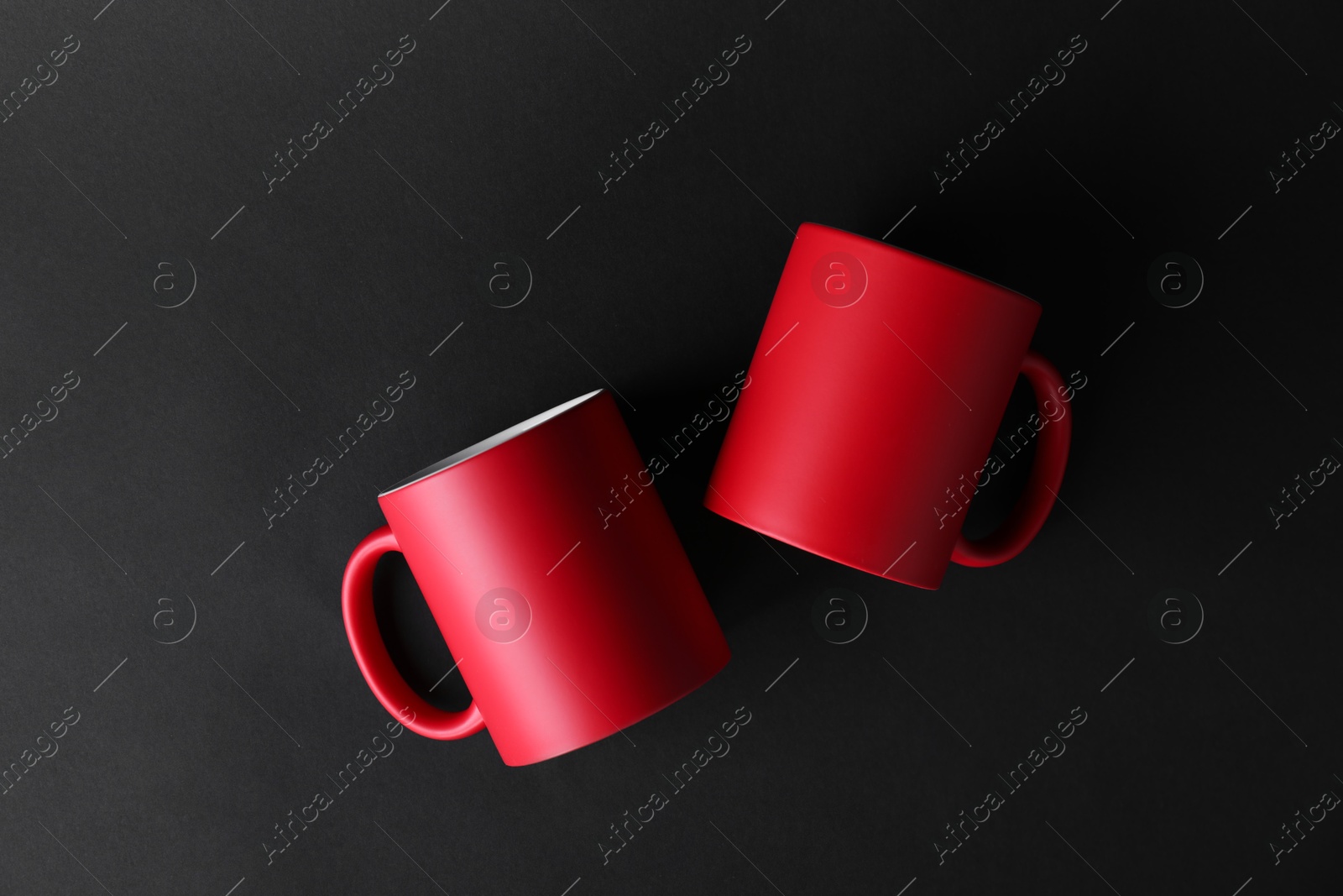 Photo of Two blank red mugs on black background, top view. Mockup for design