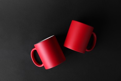 Photo of Two blank red mugs on black background, top view. Mockup for design