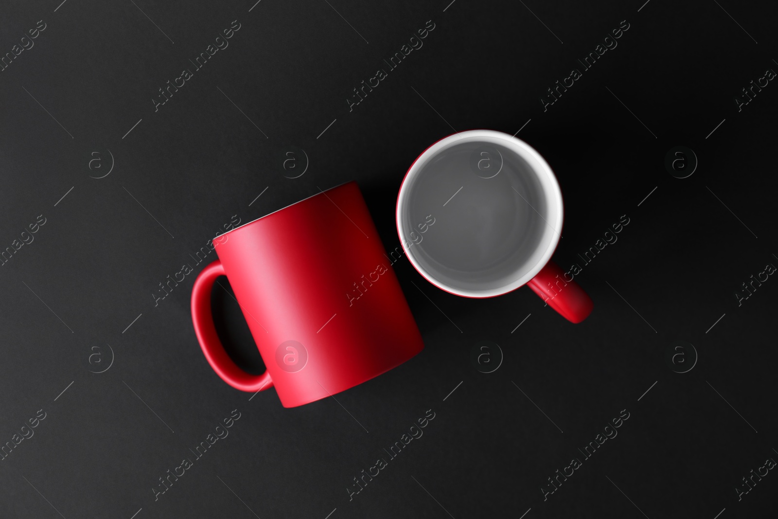 Photo of Two blank red mugs on black background, top view. Mockup for design