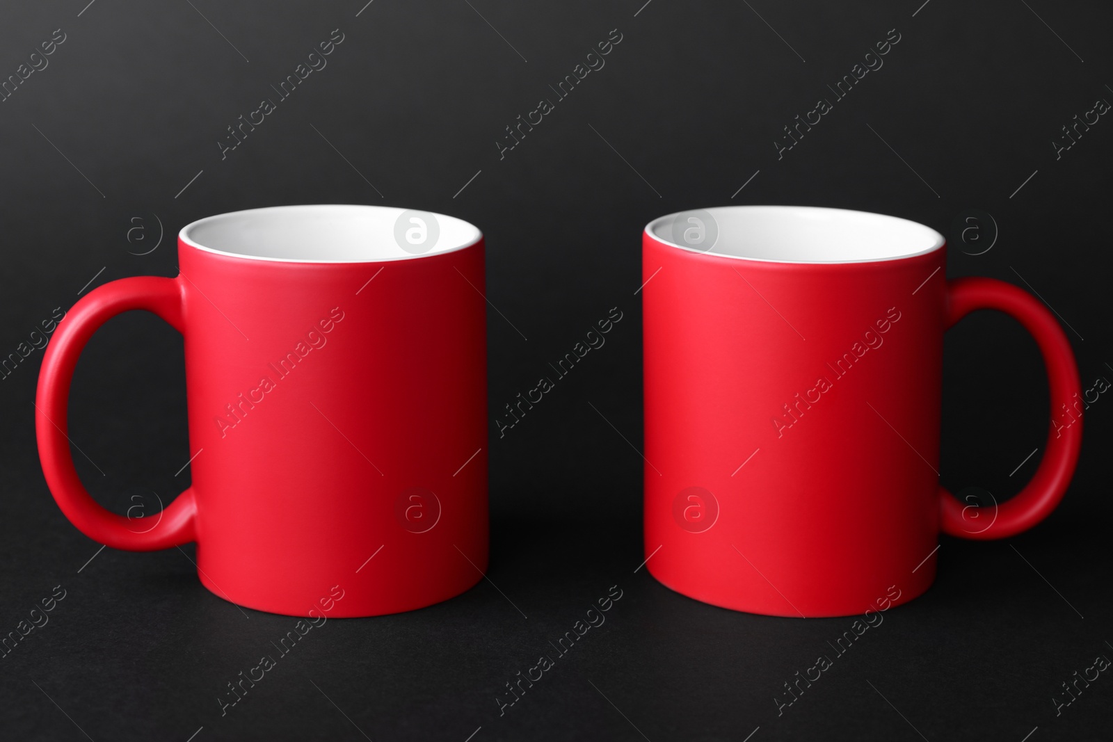 Photo of Two blank red mugs on black background. Mockup for design