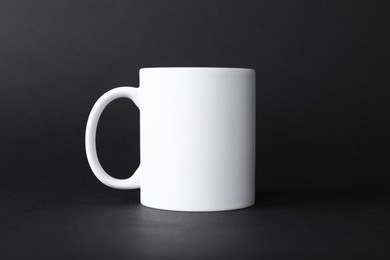 Photo of One blank white mug on black background. Mockup for design